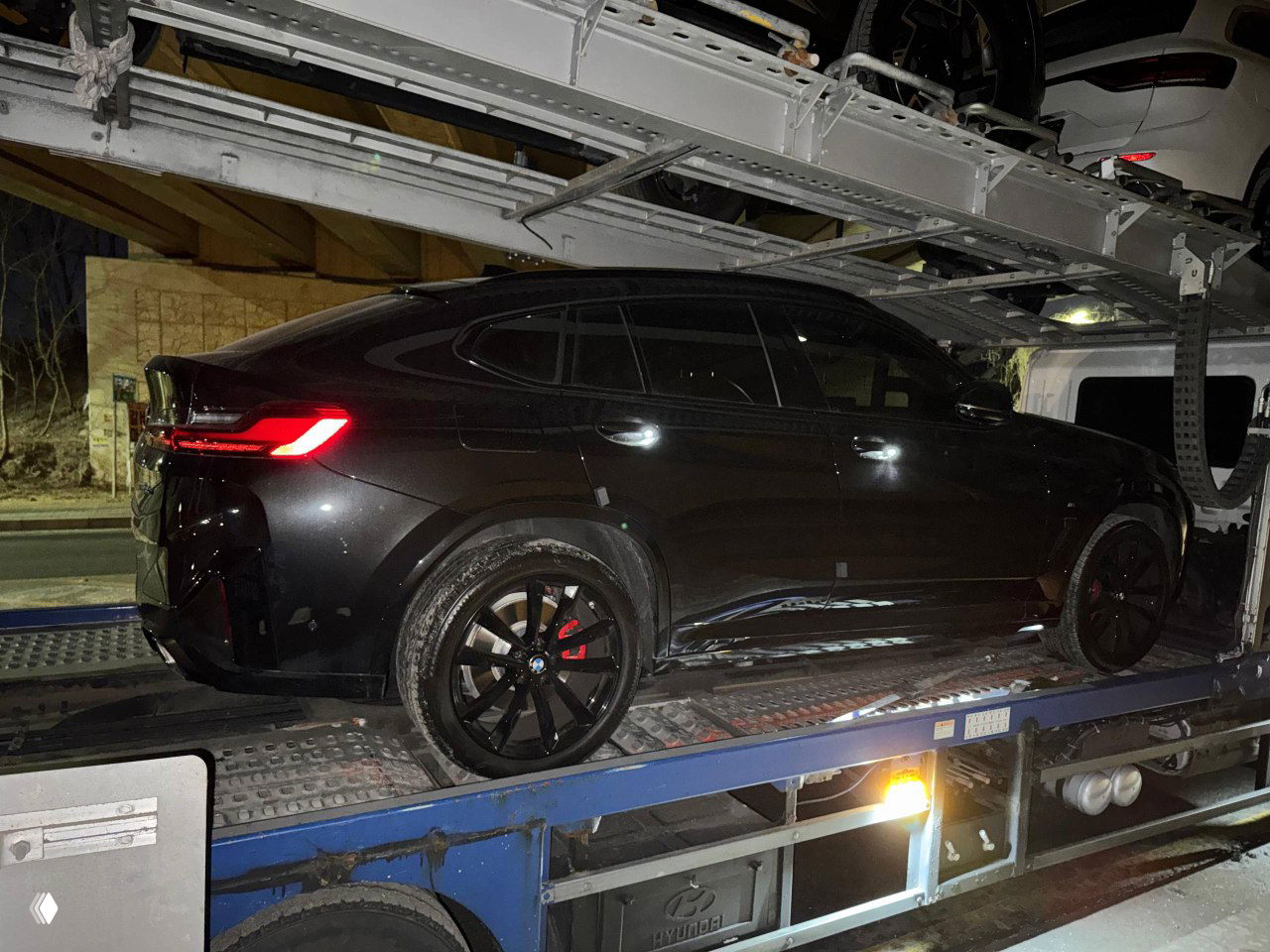 Чёрный BMW X4 размещён на палубе автовоза — боковой ракурс с подчёркнутыми колёсами и элементами кузова перед транспортировкой