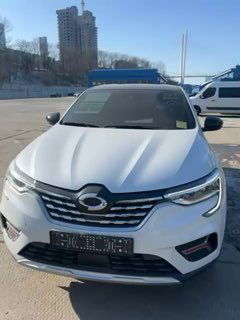 Фронтальный вид белого кроссовера Samsung XN3 на стоянке у порта/таможни, видна решётка радиатора, бампер и другие машины на фоне.