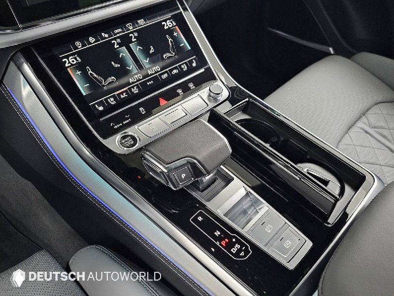 Крупный план центральной консоли Audi Q8 с сенсорными экранами, селектором передач и декоративной подсветкой в зоне переднего подлокотника