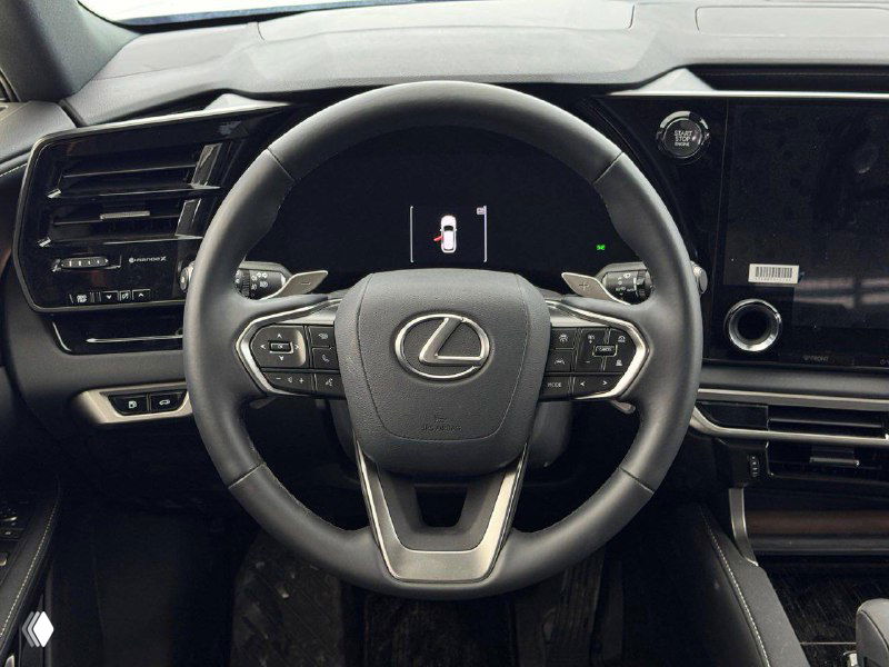 Крупный план руля Lexus RX 300 2025 с фирменным логотипом на центральной части, кнопками управления и индикаторами на приборной панели.