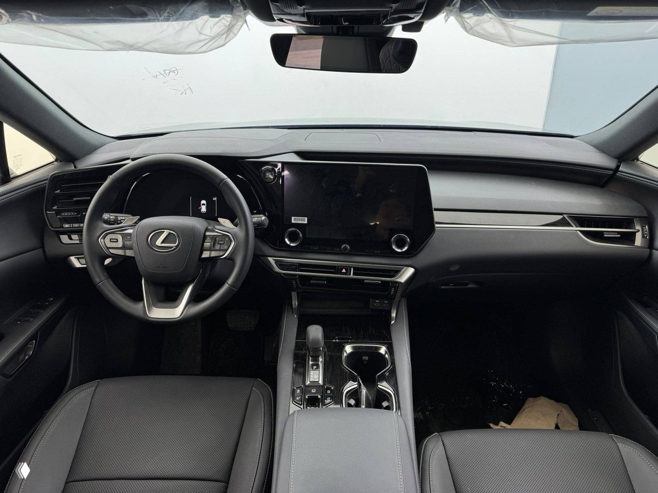 Крупный план рулевого колеса Lexus RX 300 2026 с логотипом Lexus, кнопки управления на руле и электронная приборная панель в фоне.