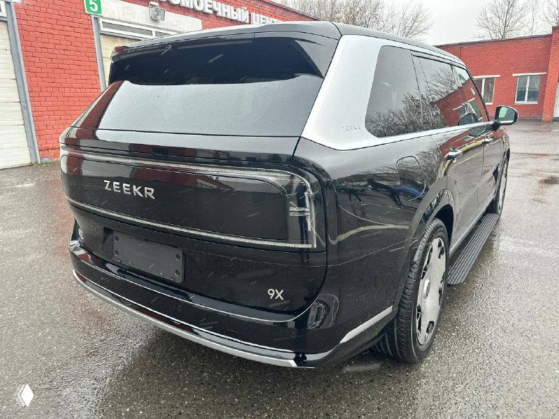 Вид сзади чёрного Zeekr 9X: тёмные фонари, логотип ZEEKR и чистые панели на фоне автомойки в дождливую погоду.