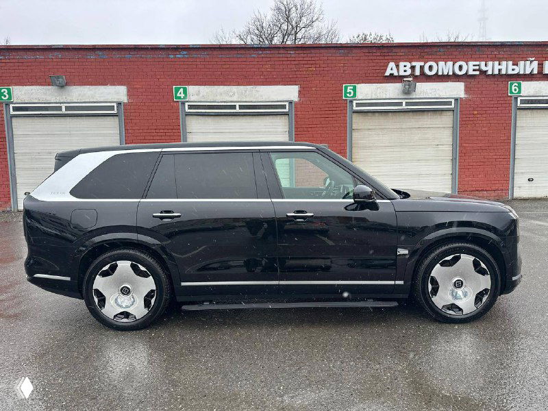 Боковой вид автомобиля Zeekr 9X вдоль стены автомойки: чёрный кузов с серебристой декоративной панелью у стойки и крупными дисками.