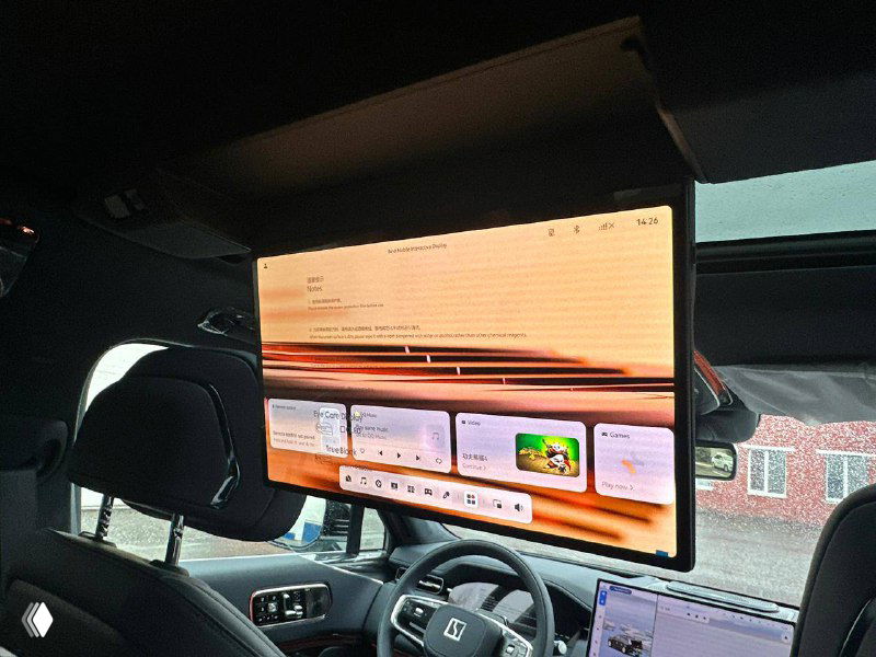 Большой потолочный монитор, развернутый для задних пассажиров, на фоне передней панели Zeekr 9X; видно интерфейс мультимедиа и часть салона.