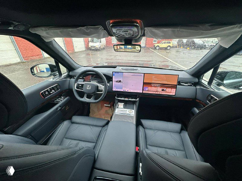 Вид салона спереди: цифровая панель, центральный большой экран, двухзонные сиденья и современная приборная панель Zeekr 9X в мокрый день.