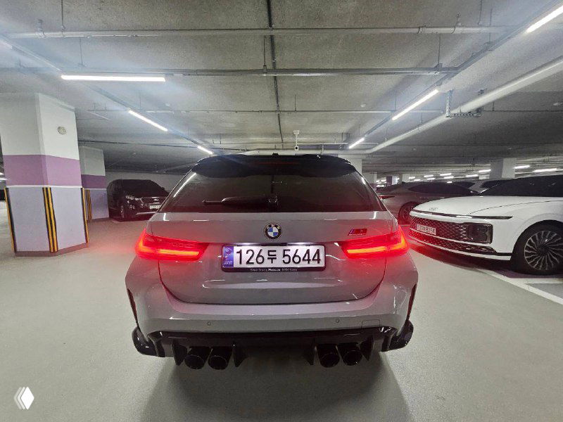 Вид сзади BMW M3 XDRIVE Touring в подземной парковке, видны яркие задние фонари, спортивный диффузор и регистрационный номер.