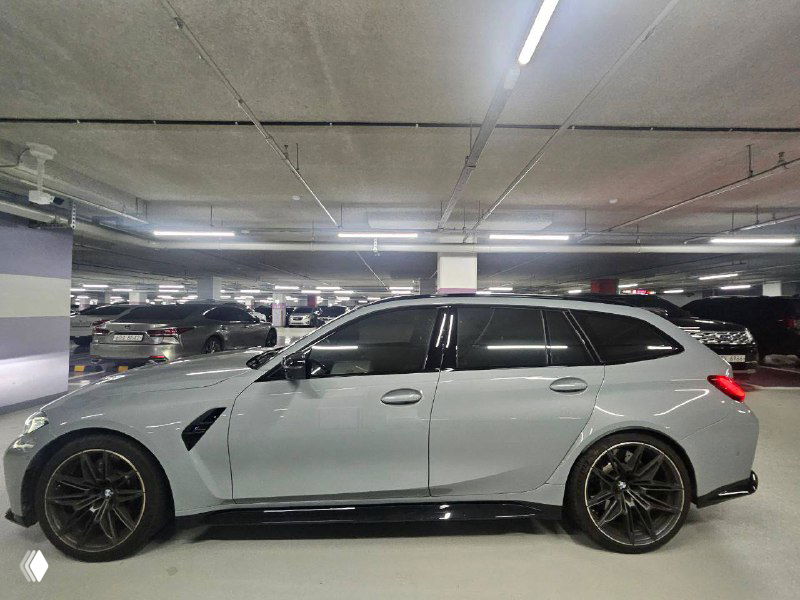 Профиль BMW M3 XDRIVE Touring в подземном паркинге, акцент на спортивных колёсах, линии кузова и дорожном клиренсе универсала.