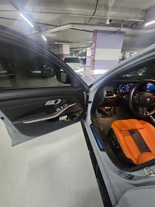 Открытая передняя дверь BMW M3: вид на панель, порог, облицовку двери и часть рулевого управления в серебристом кузове.