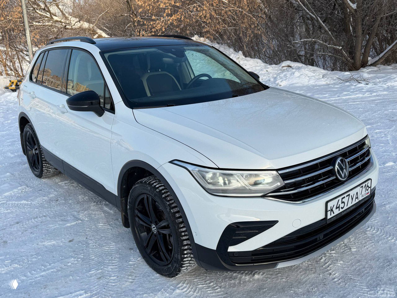Ещё один трёхчетвертной вид белого Volkswagen Tiguan Urban Sport 2022, чёрная крыша и контрастные детали, видна чистая лакокрасочная поверхность и защитная плёнка.