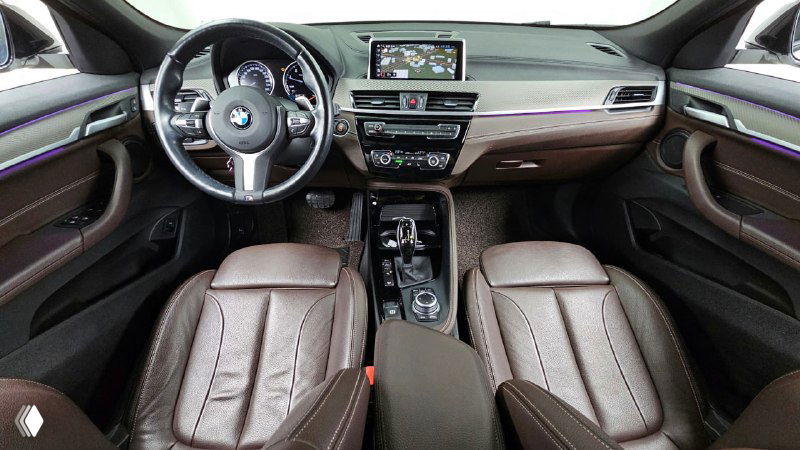 Салон BMW X2: панель приборов, мультимедиа и руль, коричневая кожаная отделка сидений, общий вид водительской зоны автомобиля.