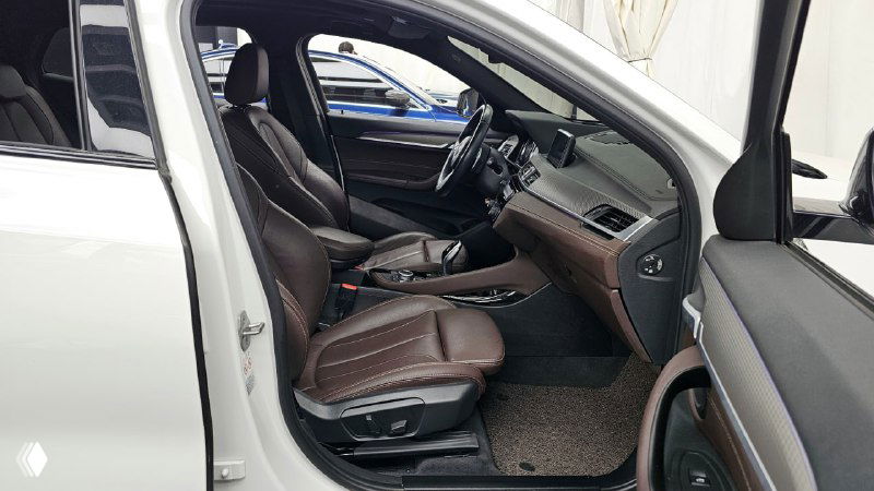 Вид на передние сиденья BMW X2 с пассажирской стороны, коричневые кресла, центральная консоль и панель управления видны в кадре.