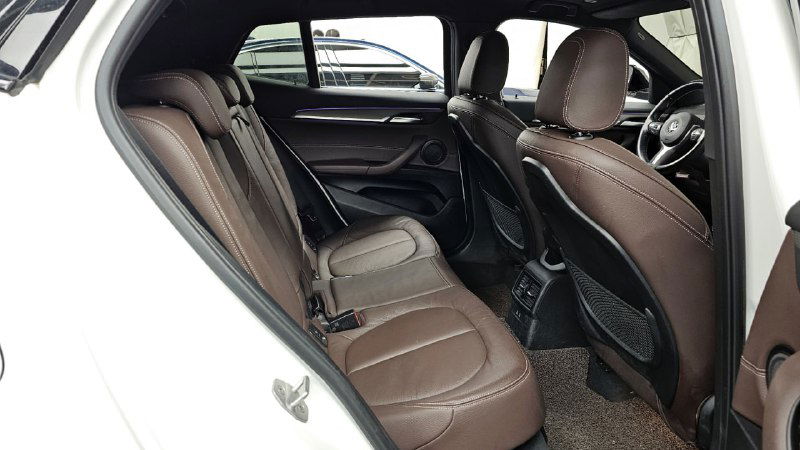 Задние сиденья BMW X2, коричневый кожаный салон, пространство для пассажиров на заднем ряду, вид через открытую заднюю дверь.