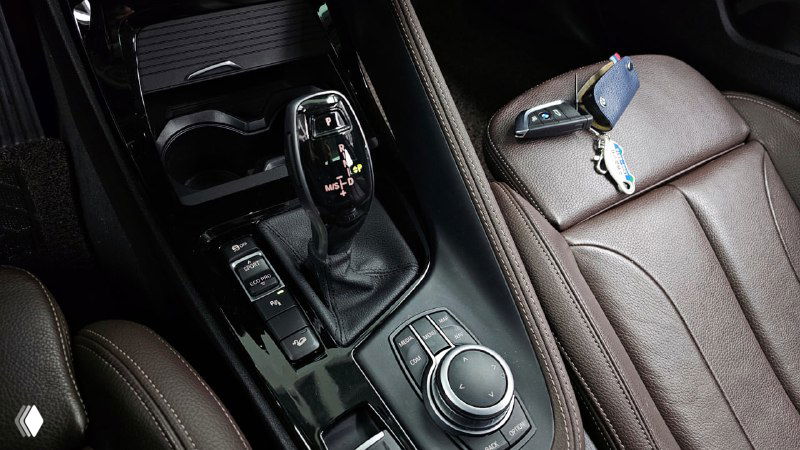 Крупный план центральной консоли BMW X2: селектор коробки передач, мультирегулятор iDrive и ключ на сиденье, детали управления показаны в кадре.