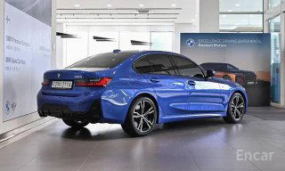 Синий BMW 3 серии G20 — вид сзади и в профиль в автосалоне, подчёркнуты линии кузова рестайлинга и оформлен номерной вставкой стенда.