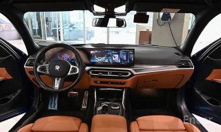 Салон BMW 3 серии G20: панель приборов, мультимедиа экран и рулевое колесо — коричневый кожаный интерьер, вид спереди из водительской зоны.