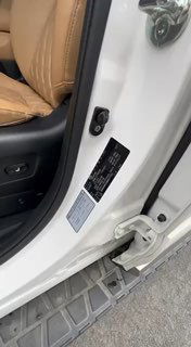 Крупный план дверного проёма белого автомобиля с видимой информационной табличкой и наклейкой на стойке, фрагмент бежевого кожаного сиденья.