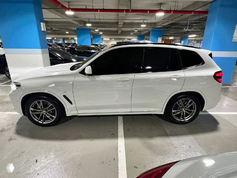 Боковой профиль белого BMW X3 xDrive 20i M Sport, чёрные зеркала и тонировка, снимок выполнен в крытой стоянке, подчёркивает линии кузова.