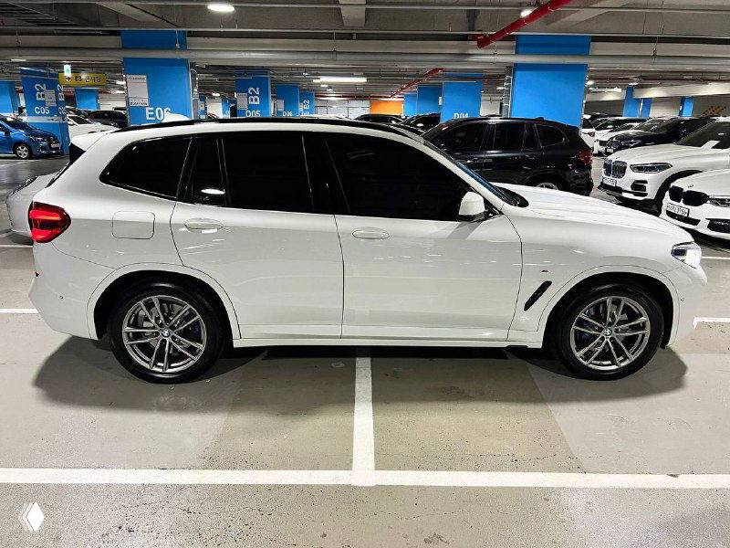 Другой боковой ракурс BMW X3 xDrive 20i M Sport белого цвета, вид с противоположной стороны в парковочном месте с разметкой на полу.