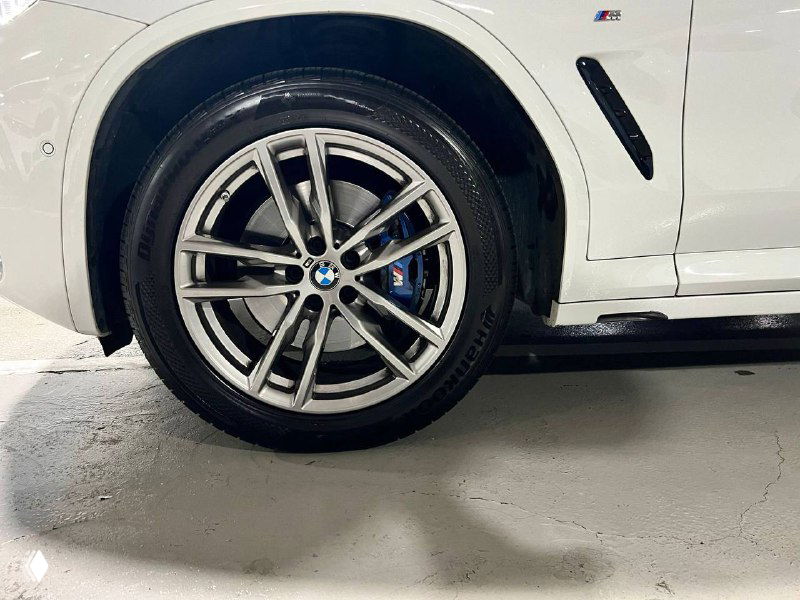 Крупный план легкосплавного диска и шины BMW X3 M Sport, вид на тормозной суппорт и рисунок диска в закрытом паркинге.