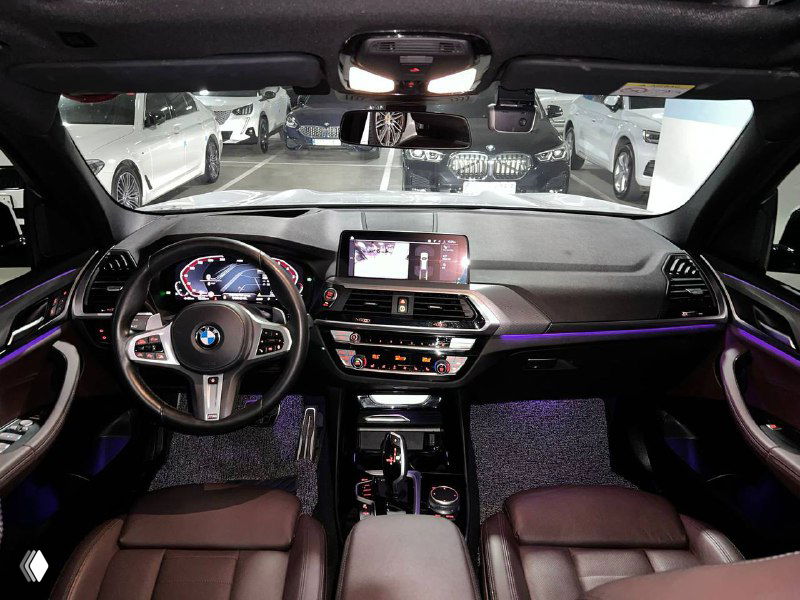 Вид салона BMW X3 с панели водителя: мультимедийный экран, руль M Sport, подсветка и коричневые кожаные сиденья — интерьер в хорошем состоянии.
