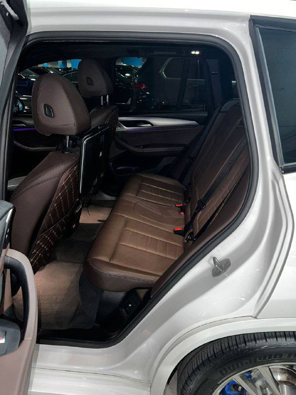 Задний ряд сидений BMW X3 в коричневой коже, прострочка и места для пассажиров, вид с открытой дверью демонстрирует пространство салона.