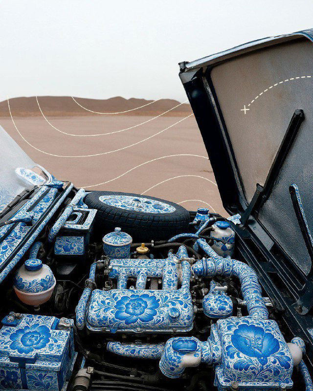 Крупный план моторного отсека автомобиля, элементы двигателя и детали покрыты бело‑синим гжельным орнаментом, декоративная роспись на технических частях.