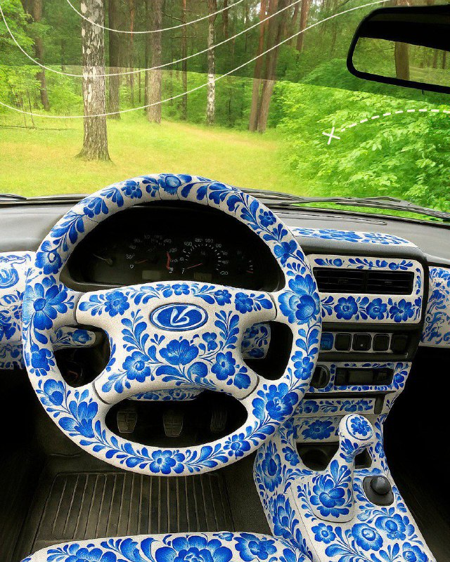 Салон автомобиля: руль, торпеда и элементы управления расписаны в бело‑синием гжельном стиле; детализация узора заметна в интерьере.