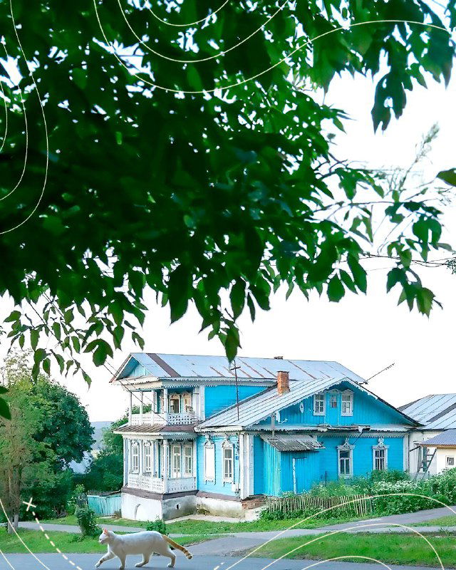 Старинный деревянный двухэтажный дом с голубой отделкой и резными деталями на фоне листвы — пример провинциальной архитектуры Тарусы.