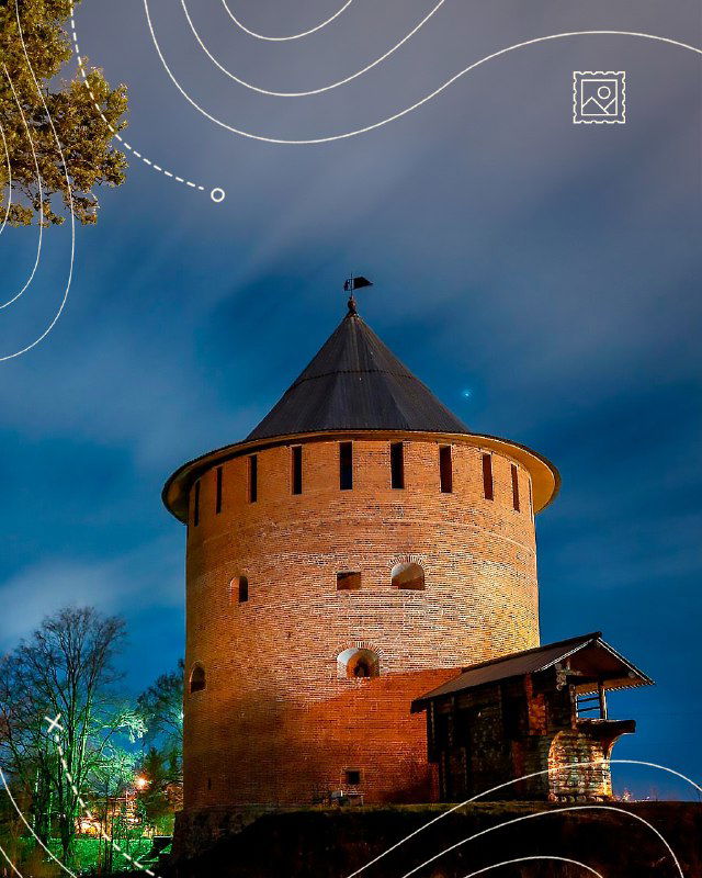 Ночная фотография одной из башен Детинца, освещённой тёплым светом; кирпичные стены и вечернее небо создают атмосферу исторической крепости.