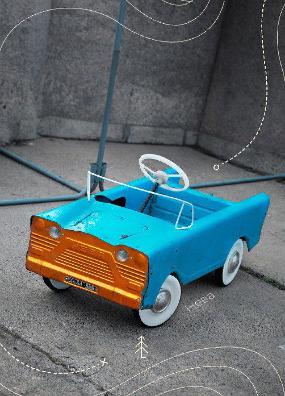 Бирюзовая педальная машина с оранжевой передней панелью, вид с трёхчетвертей на асфальтовом фоне; подчёркнут дизайн советской игрушки.
