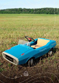 Голубой педальный родстер стоит в поле на фоне леса; фотосъёмка на открытом воздухе создаёт ностальгическое настроение путешествия.