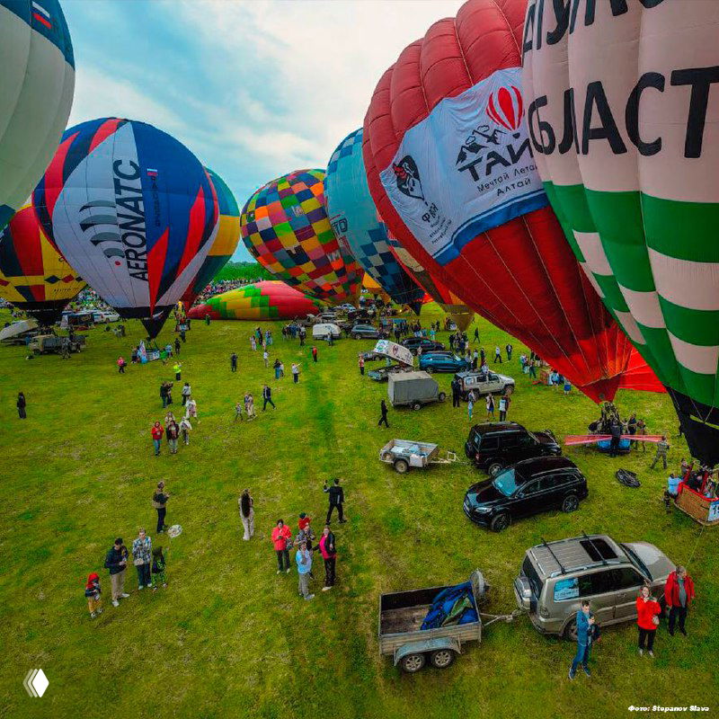 Надувание и выравнивание корзин и оболочек шаров на зеленом поле: команда, прицепы и техники перед подъёмом в небо.
