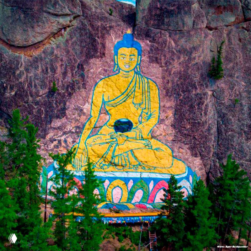 Изображение Будды на скале Баян-Хонгор в окружении хвойного леса; видно яркую окраску, контуры рисунка и природный масштаб памятника.