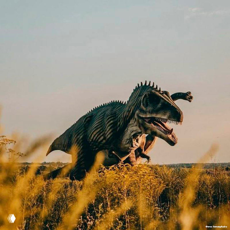 Хищная модель динозавра с раскрытой пастью и зубами в траве — атмосферный кадр заката в заброшенном динопарке на территории «Золотого города», Тульская область.