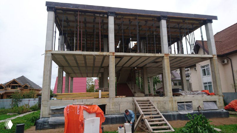 Вид со стороны на смонтированные перекрытия МАРКО и несущие колонны: несколько этажей после установки перекрытий и строительные леса рядом.