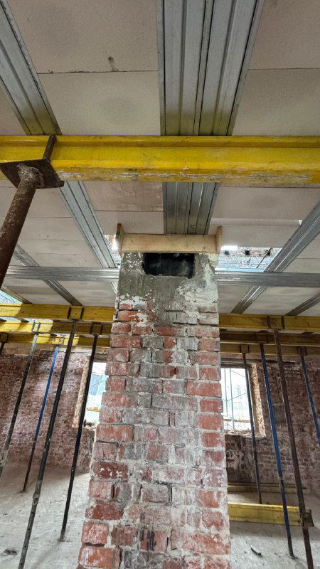 Горизонтальный вид собранных облегчённых панелей перекрытия и подпорок над кирпичной стеной в процессе реконструкции многолетнего общежития.