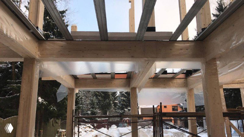 Строительные работы внутри деревянного дома: деревянные балки и сборно-монолитные панели в процессе установки перекрытия в зимних условиях на объекте.