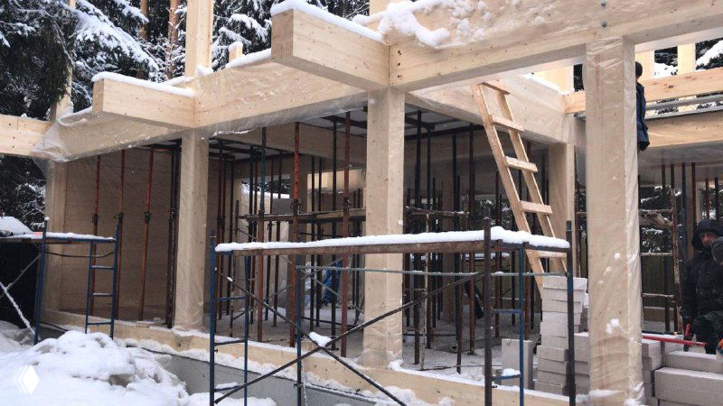 Опалубка, леса и временные опоры вокруг деревянных колонн во время монтажа монолитного перекрытия — подготовительный этап на объекте в снегопаде.