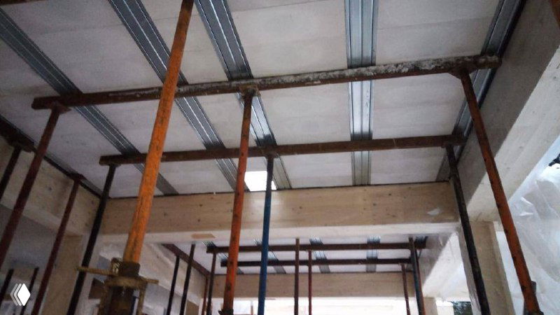 Вид снизу на монолитное перекрытие: металлические направляющие, подпорки и элементы армирования перед заливкой бетонной плиты в деревянном доме.