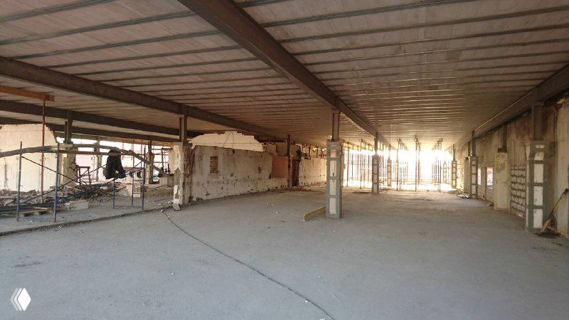 Просторный внутренний объём первого этажа до перепланировки: пустое помещение с бетонным полом, опорами и видимыми потолочными конструкциями и сетями освещения.