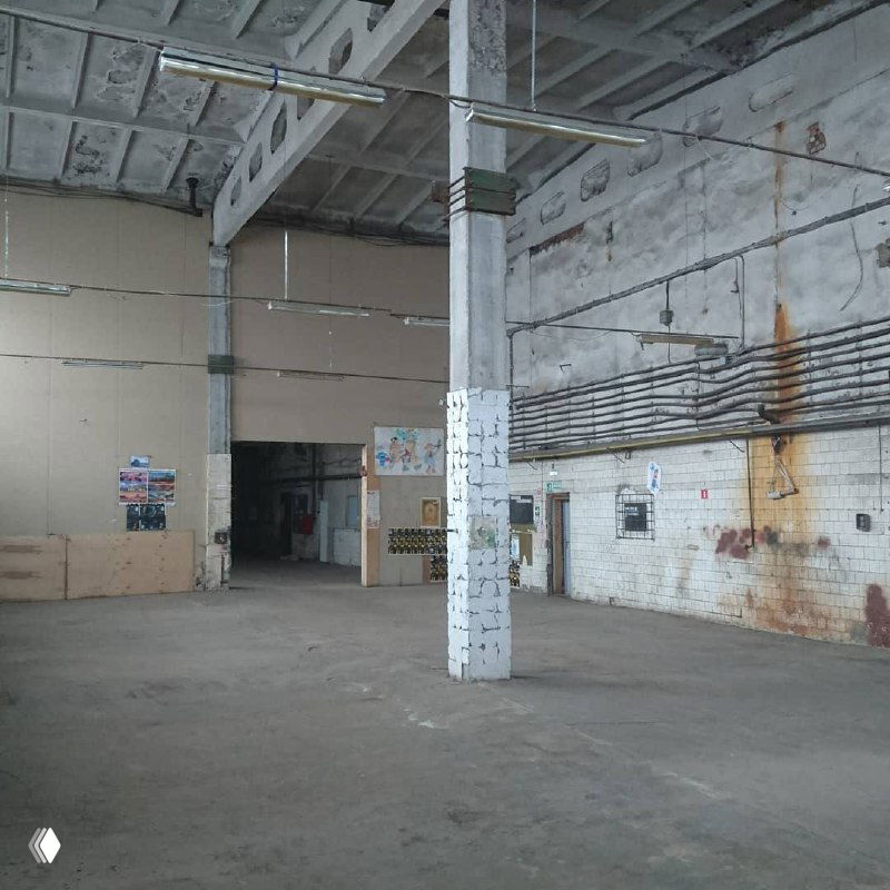 Внутренний вид цеха с опорными колоннами и высокими стенами, видно существующие инженерные трассы и следы прежней эксплуатации перед реконструкцией.