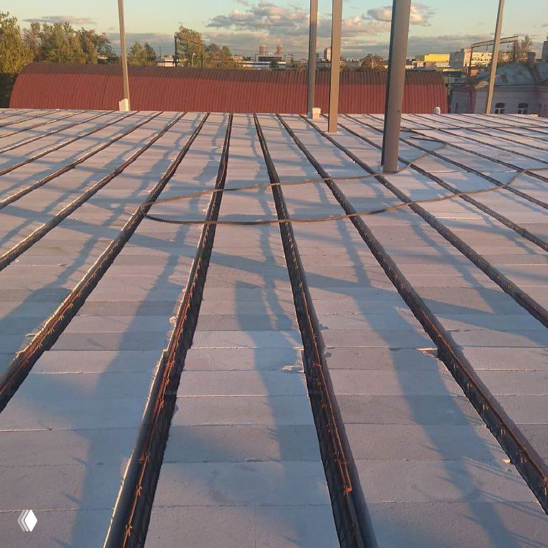 Крыша с видимыми рядами часторебристых плит и прогонами, солнечный вечерний свет подчёркивает рёбра перекрытий и монтажные швы перед отделкой.