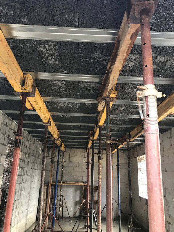 Интерьерный кадр со снятым видом перекрытия снизу: металлические балки и блоки, временные опоры и внутренние стены из блоков.