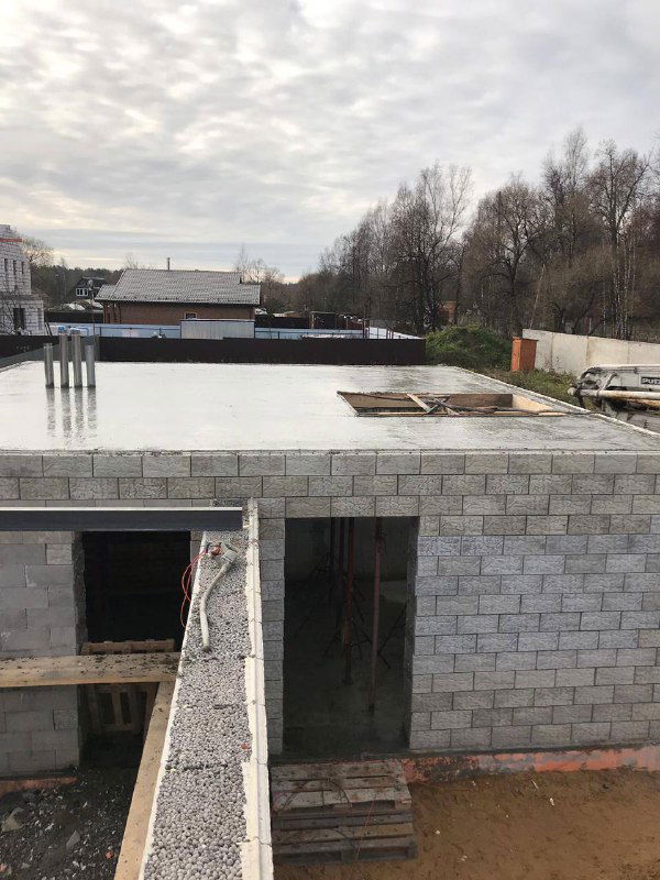 Внешний вид дома с завершённым монолитным перекрытием: ровная плита и вид на фасад и участок вокруг стройплощадки.