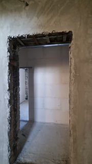 Внутренний проём в здании после работ: вид на дверной проём без отделки, оштукатуренные стены, бетонный пол и открытая потолочная зона в помещении.