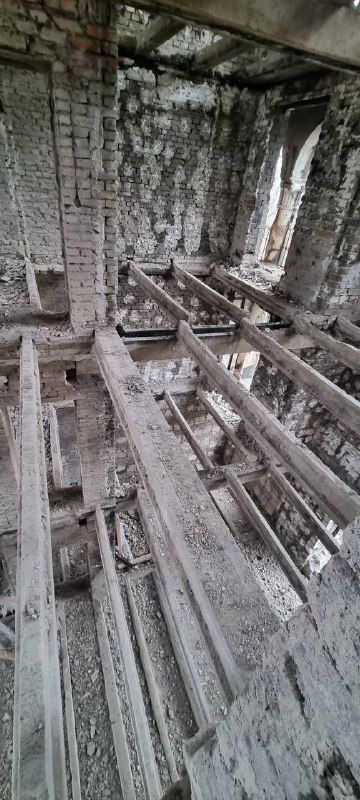 Вид изнутри разрушенного здания: балки перекрытия частично утрачены, видны остатки конструкций и мусор на полу, показано состояние до восстановления.