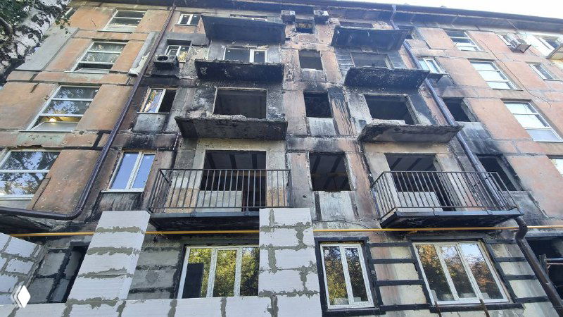 Фрагмент жилого дома с выгоревшими балконами и следами ремонта на первом плане: совмещение восстановленных и повреждённых участков фасада.