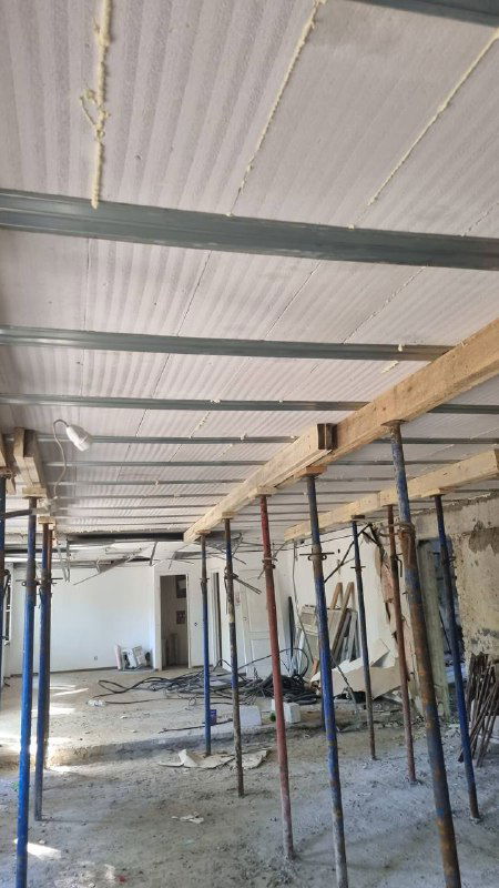 Временные опоры и металлические элементы под установленными перекрытиями в помещении на этапе реконструкции; вид на внутренние монтажные работы.
