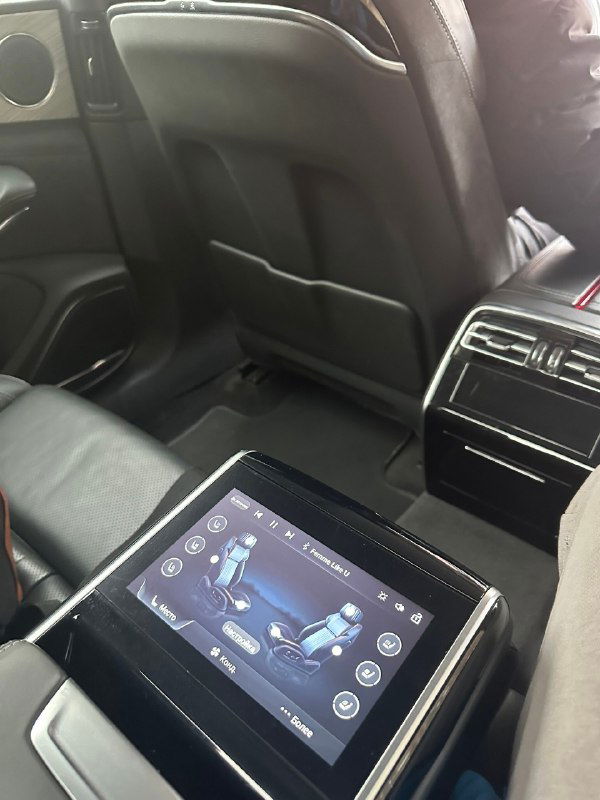 Интерьер заднего сиденья автомобиля с сенсорной панелью на подлокотнике; демонстрация удобств и цифрового управления комфортом.