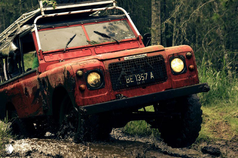 Красный внедорожник, проехавший через грязь и лесную тропу, ракурс подчёркивает следы активной езды и преодоление препятствий.